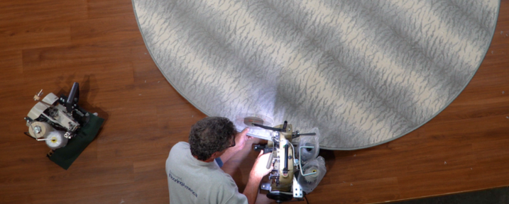 Man working on the edging of a circular grey are rug